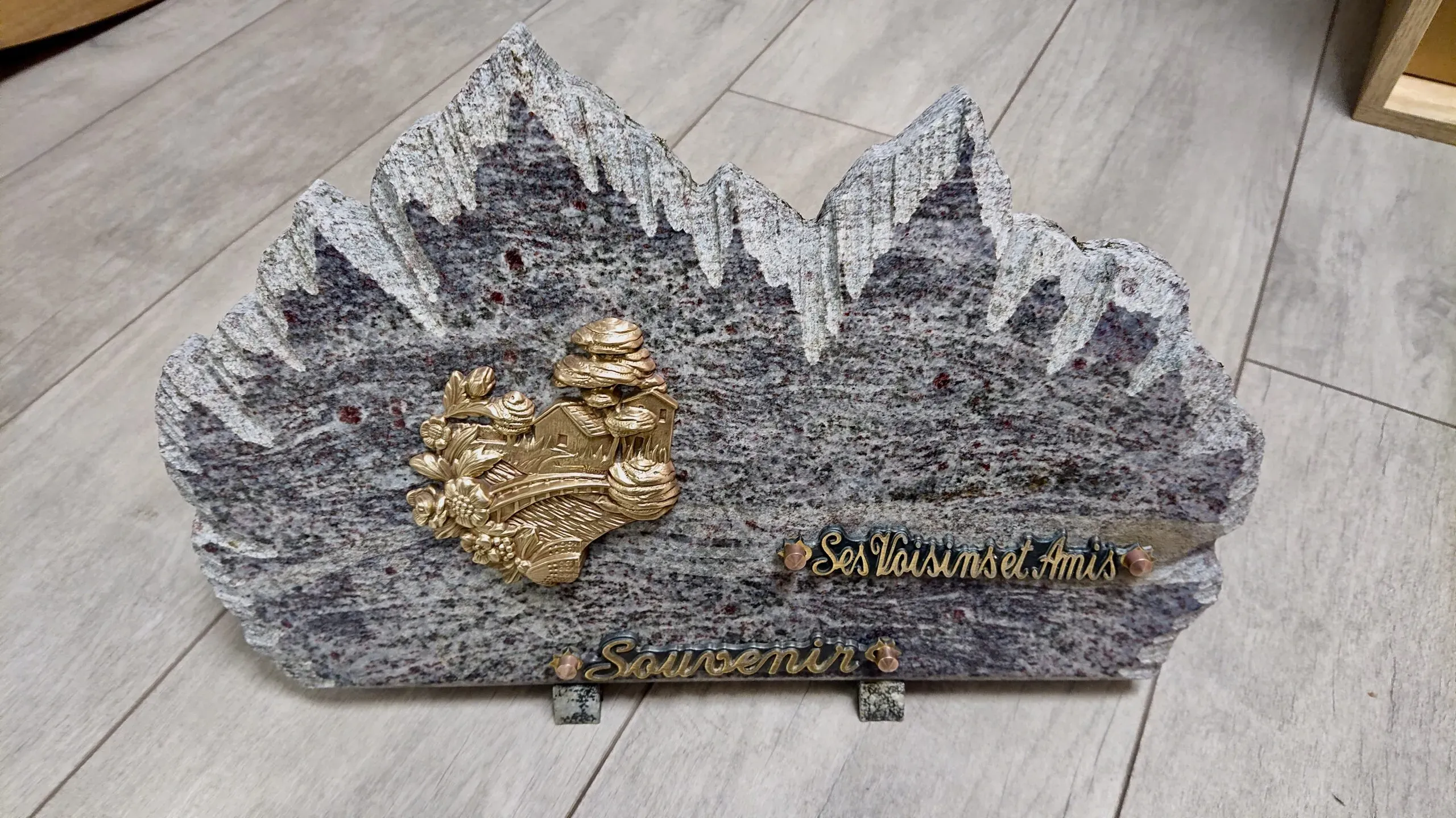 Plaque funéraire en granit en forme de montagne avec décorations en bronze.