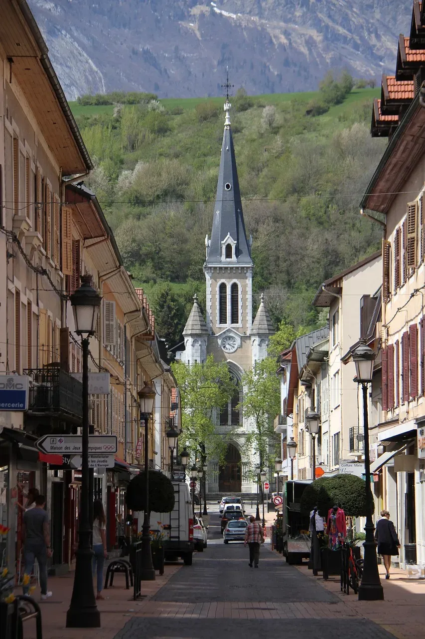 Rue commerçante du centre-ville menant à une église au clocher pointu.